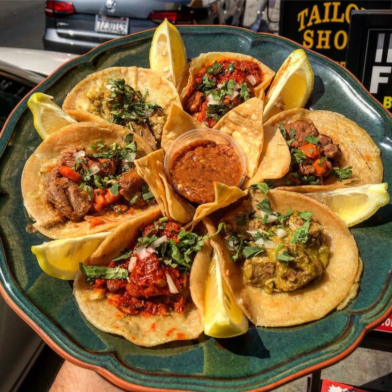 A platter of Cilantro Lime tacos with various fillings, cilantro, onions, and lemon wedges.