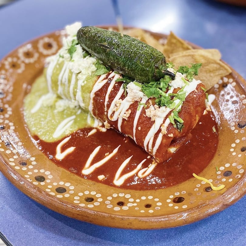 A Cilantro Lime burrito, topped with red and green sauce, cheese, cilantro, and a whole jalapeño.